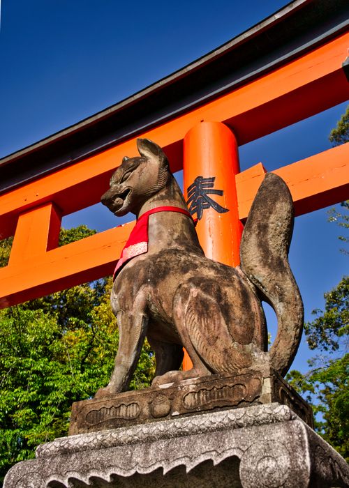 Free Stone fox statue at Fushimi Inari Shrine in Kyoto, Japan, under a clear blue sky. Stock Photo