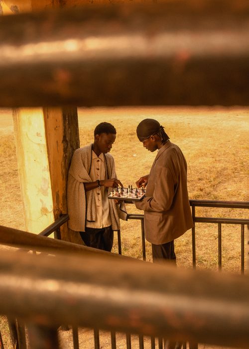 Free Two men playing chess on a balcony in Ado Ekiti, Nigeria, observed through railings. Stock Photo