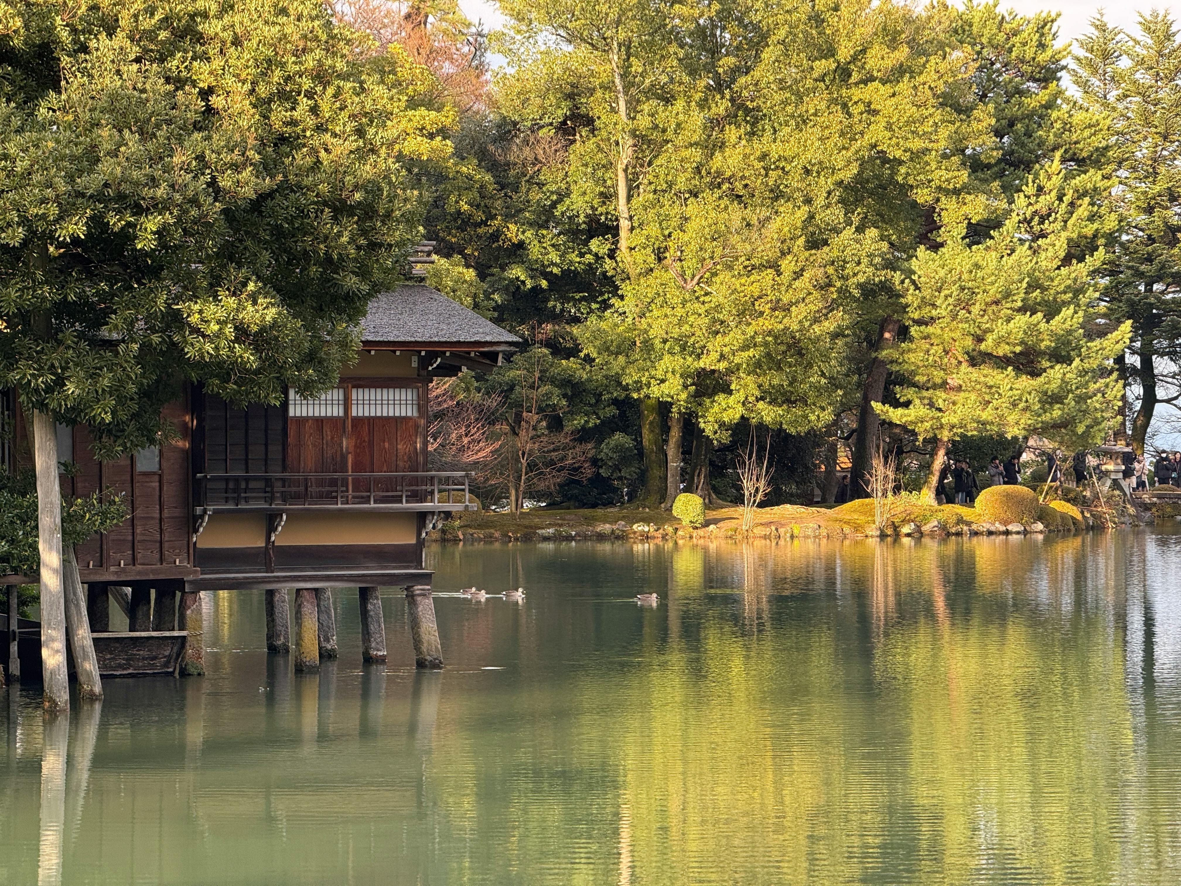 Serene view of Japanese lakeside with traditional architecture and lush greenery.