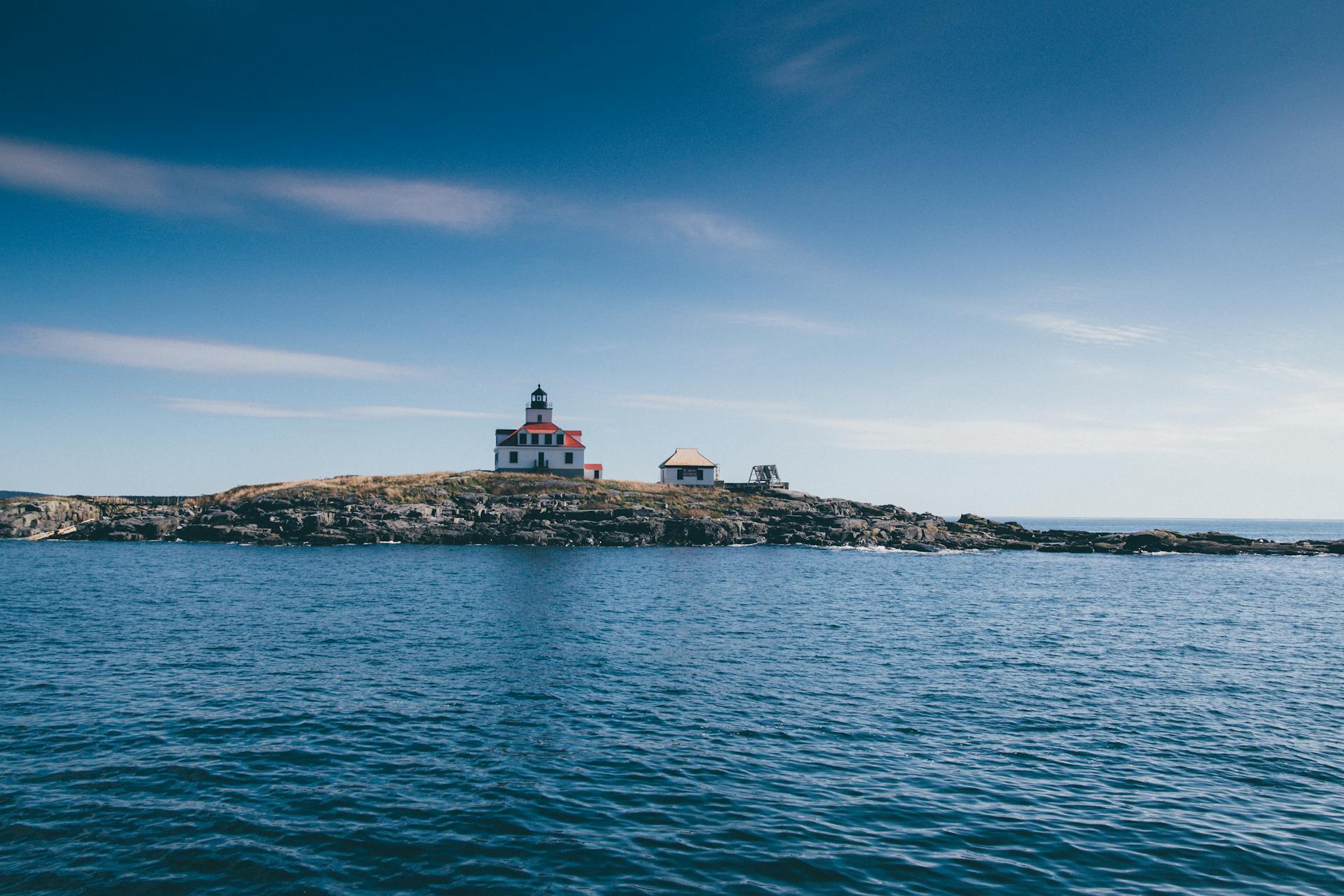 A picturesque lighthouse on a rocky island surrounded by the ocean under a clear blue sky.