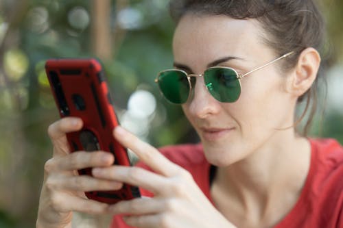 Free Woman Holding Smartphone and Wearing Sunglasses Stock Photo