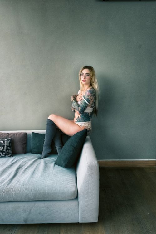 Free Woman with tattoos poses confidently in a modern living room setting. Stock Photo