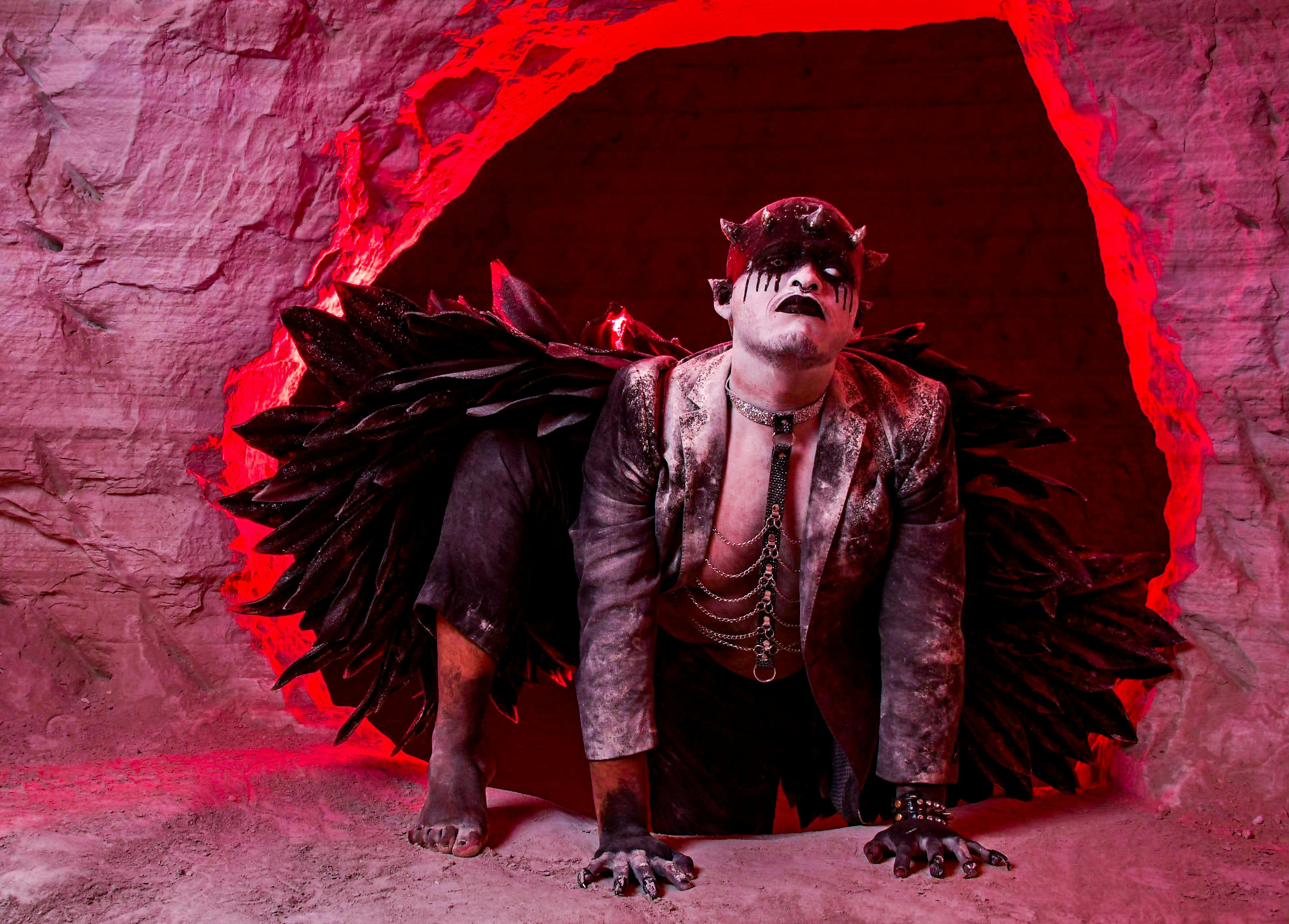 Free A fantasy character in dark costume emerges from a red-lit cave, creating a dramatic and surreal atmosphere. Stock Photo