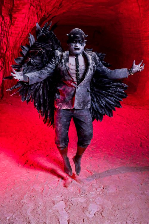 Free A dramatic shot of a dark angel figure in a red-lit cave, wearing black wings and gothic attire. Stock Photo