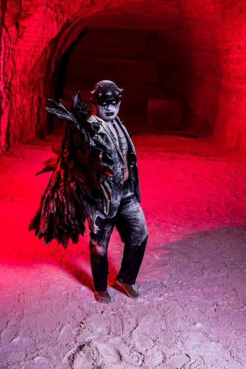 Free A performer with dramatic costume and makeup stands in a red-lit cave. Unique, artistic atmosphere. Stock Photo