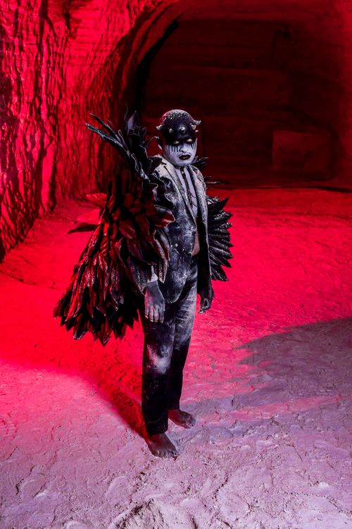 Free Mysterious figure with dark costume and makeup stands in a cave with striking red lighting. Stock Photo