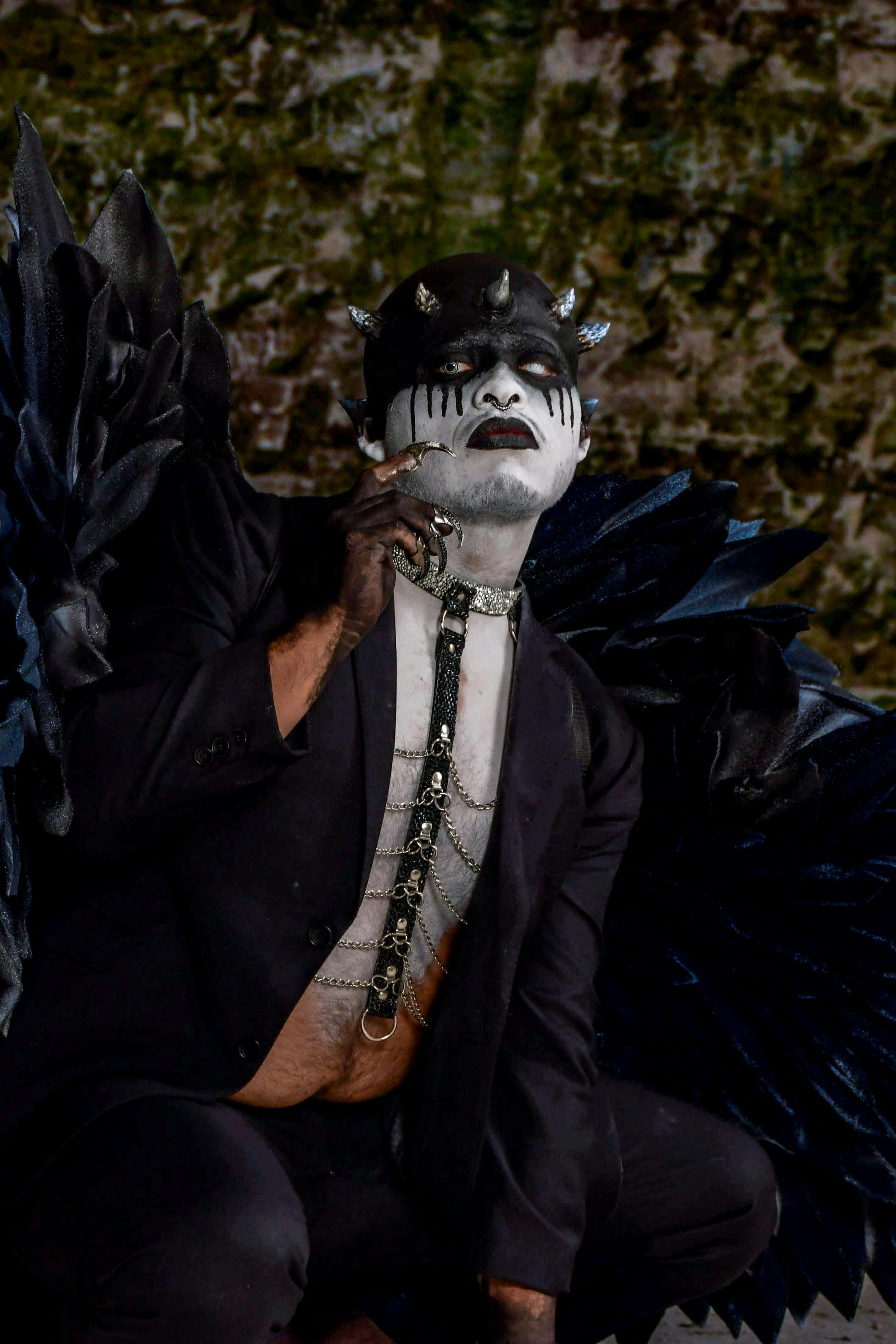 Man in gothic attire with bold makeup and dark wings, creating a dramatic look.