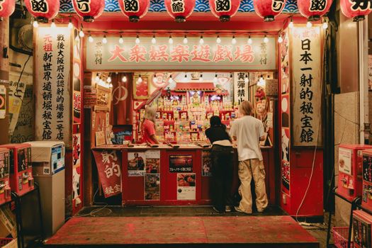 A vibrant Japanese arcade stall with lanterns and people enjoying games at night.