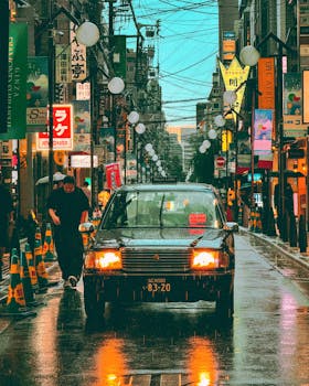 A moody street view in Tokyo with neon lights reflecting on wet pavement during rain.