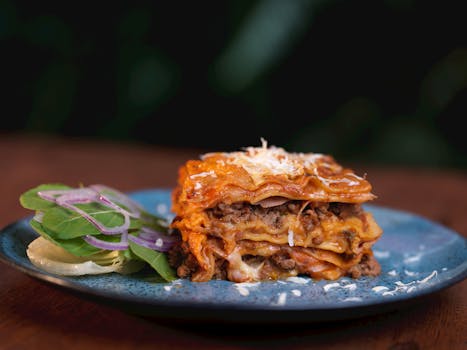 Close-up of a delicious homemade lasagna served with fresh salad on a ceramic plate.