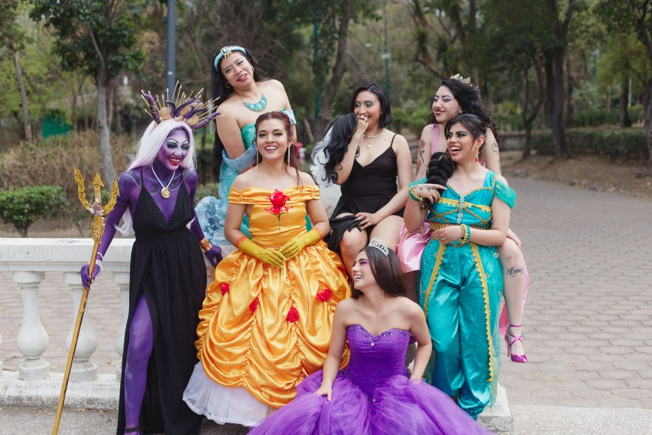 Seven women dressed in vibrant, detailed cosplay costumes enjoying a sunny day outdoors.