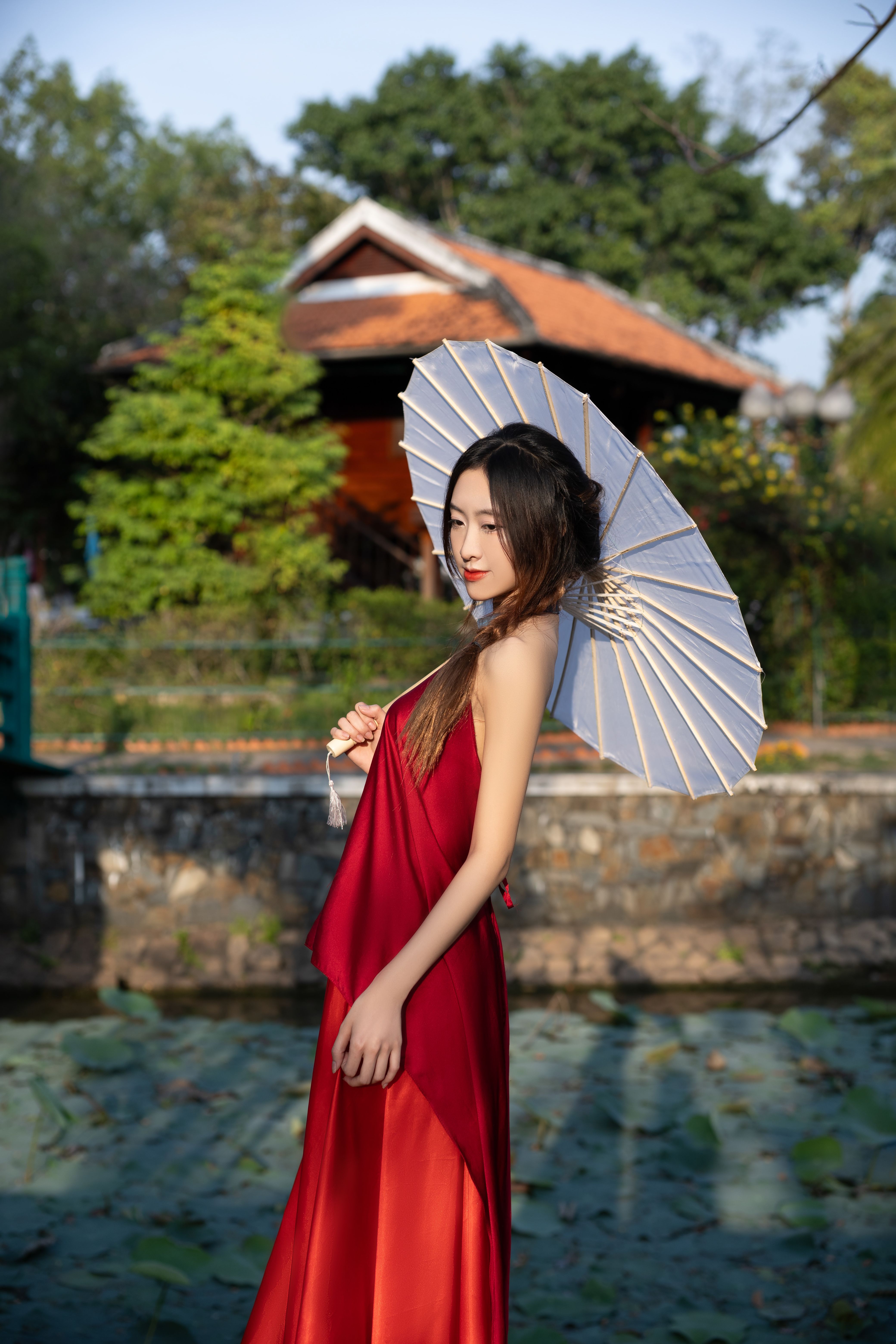 Elegant woman in a red dress holding a parasol in a lush garden setting.