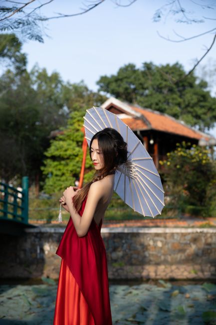 A woman in a red dress holds a parasol outdoors, blending traditional and modern styles.