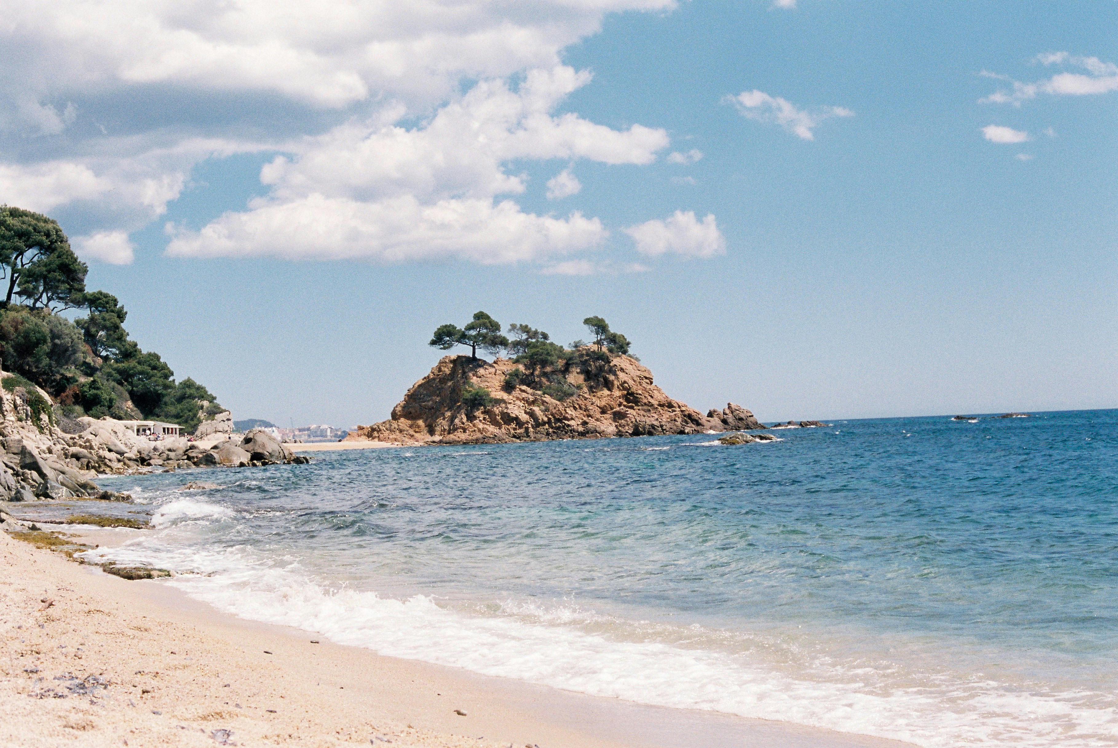 Serene beach and rocky island under bright sky, perfect for travel inspiration.