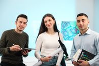 Three young adults discussing and collaborating in a modern office setting.