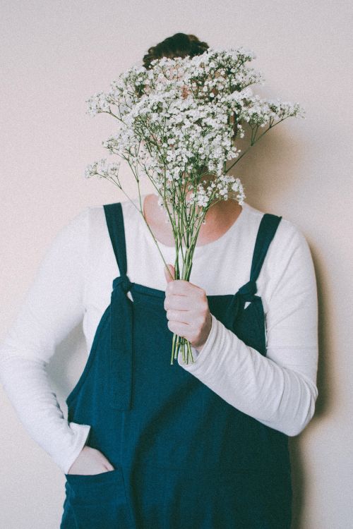 Free A person in overalls holding a bouquet of baby's breath flowers indoors. Stock Photo