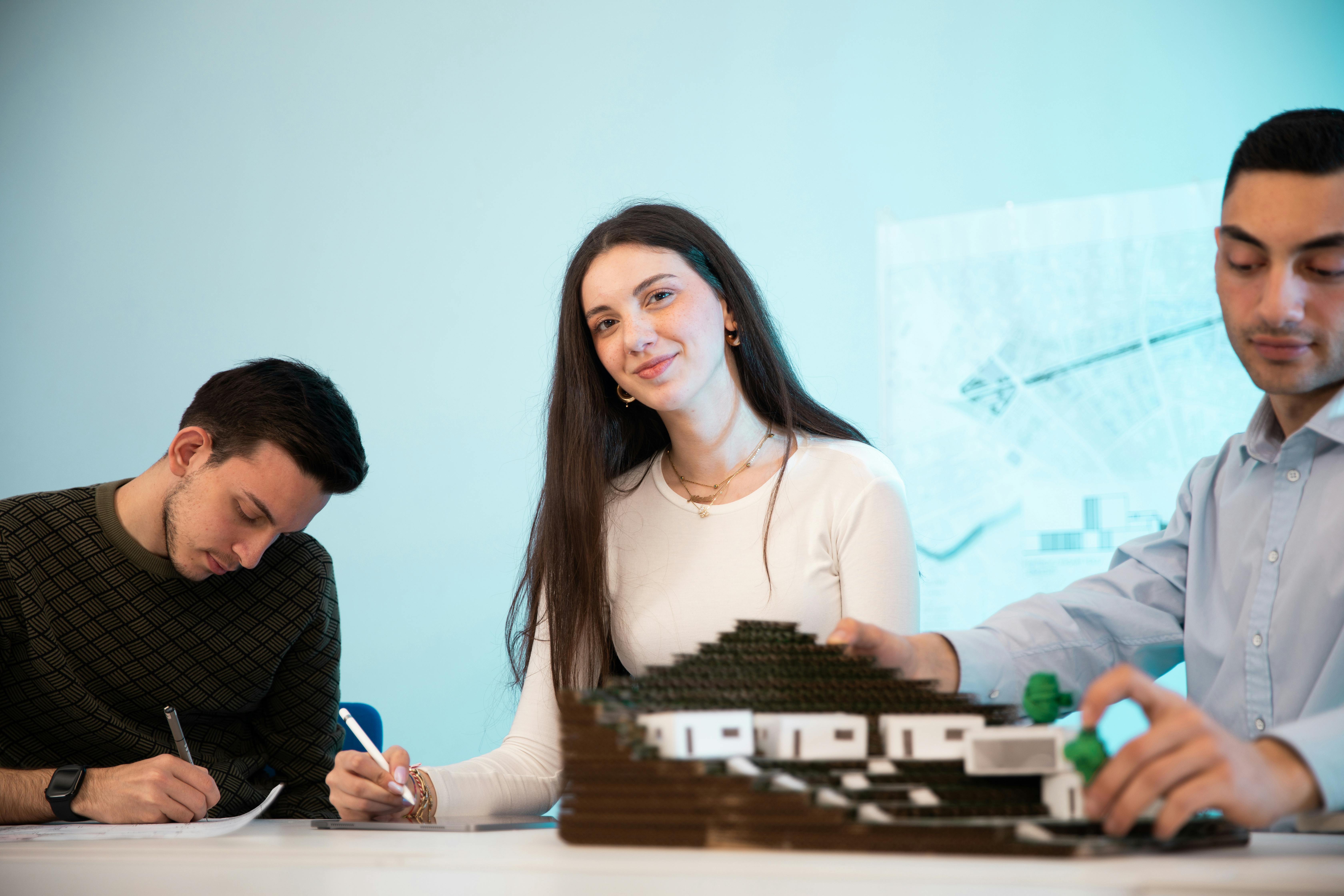 Zadarmo Traja ľudia spolupracujúci na architektonickom modeli v kancelárskom prostredí s dôrazom na tímovú prácu. Fotka z fotobanky