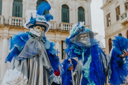 Free Bright Venetian costumes at the carnival in Italy, featuring intricate masks and vibrant blue and silver fabrics. Stock Photo