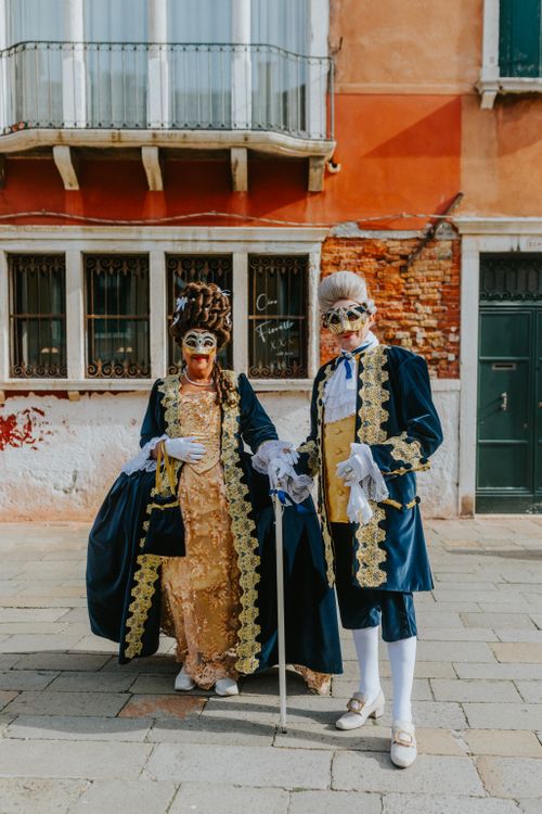 Free Costumed couple in traditional Venetian attire with masks, posing outdoors in Venice. Stock Photo