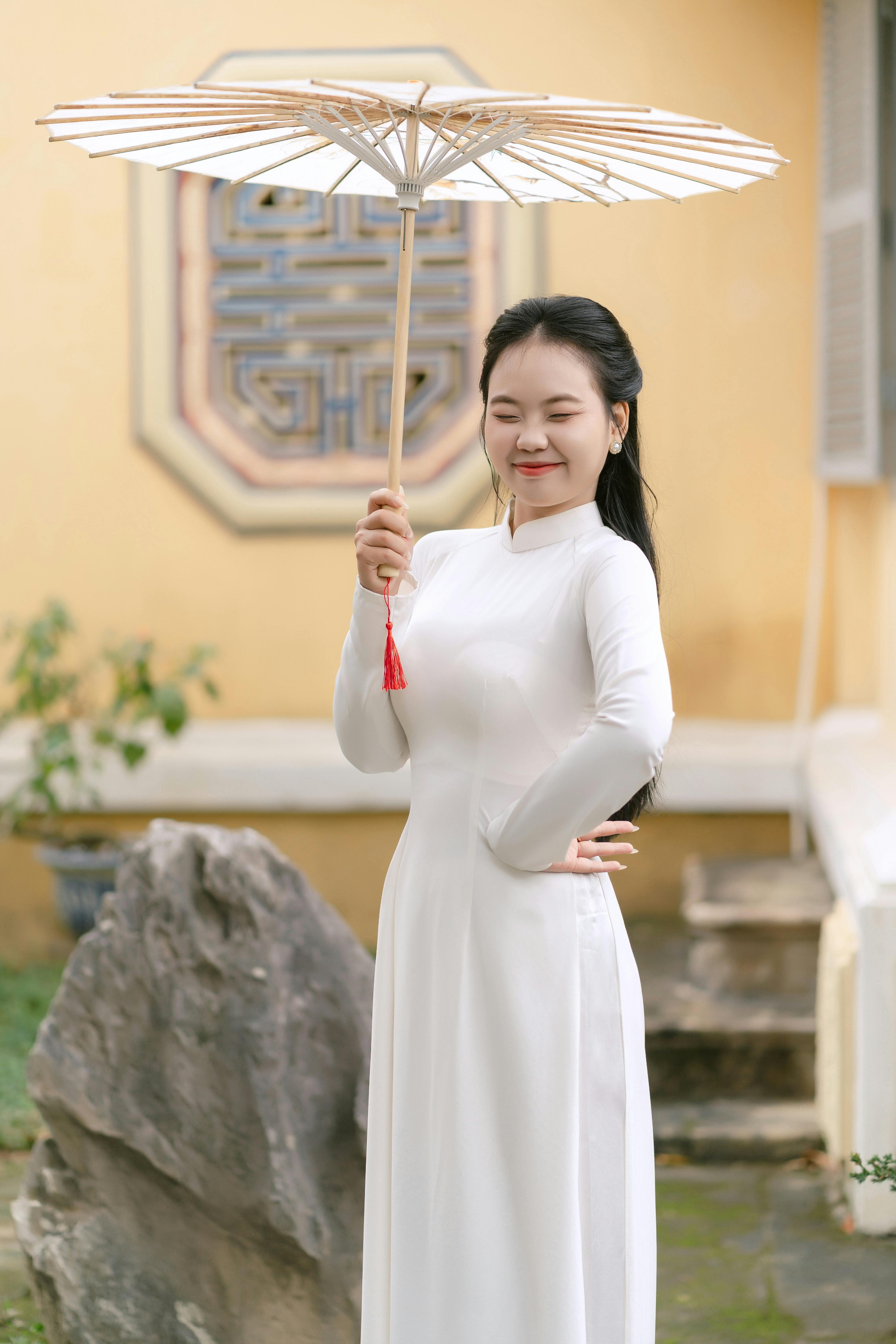 Asian woman holding an umbrella, wearing a traditional Vietnamese Ao Dai dress outdoors.