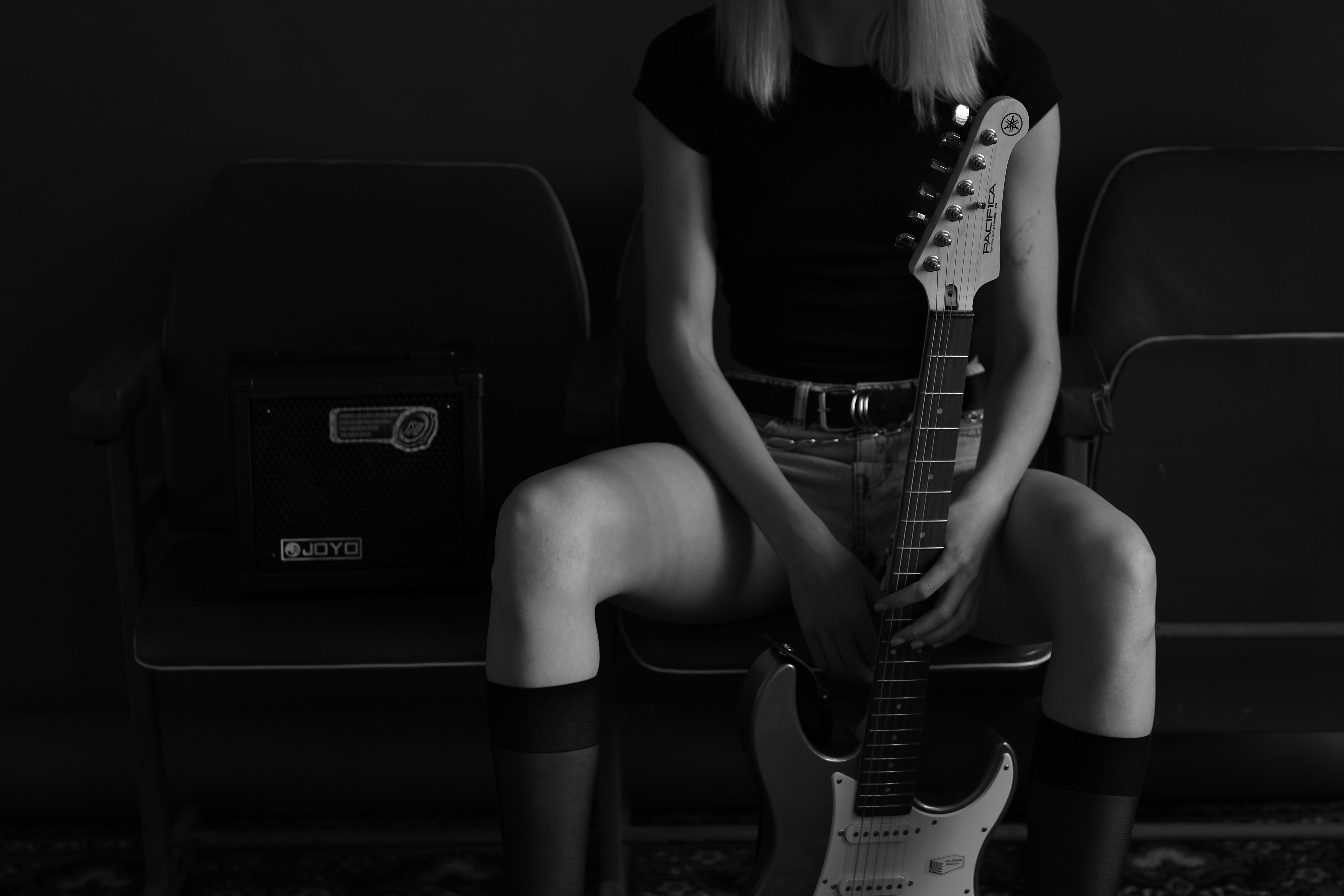 Moody black and white photo of a person sitting with an electric guitar.