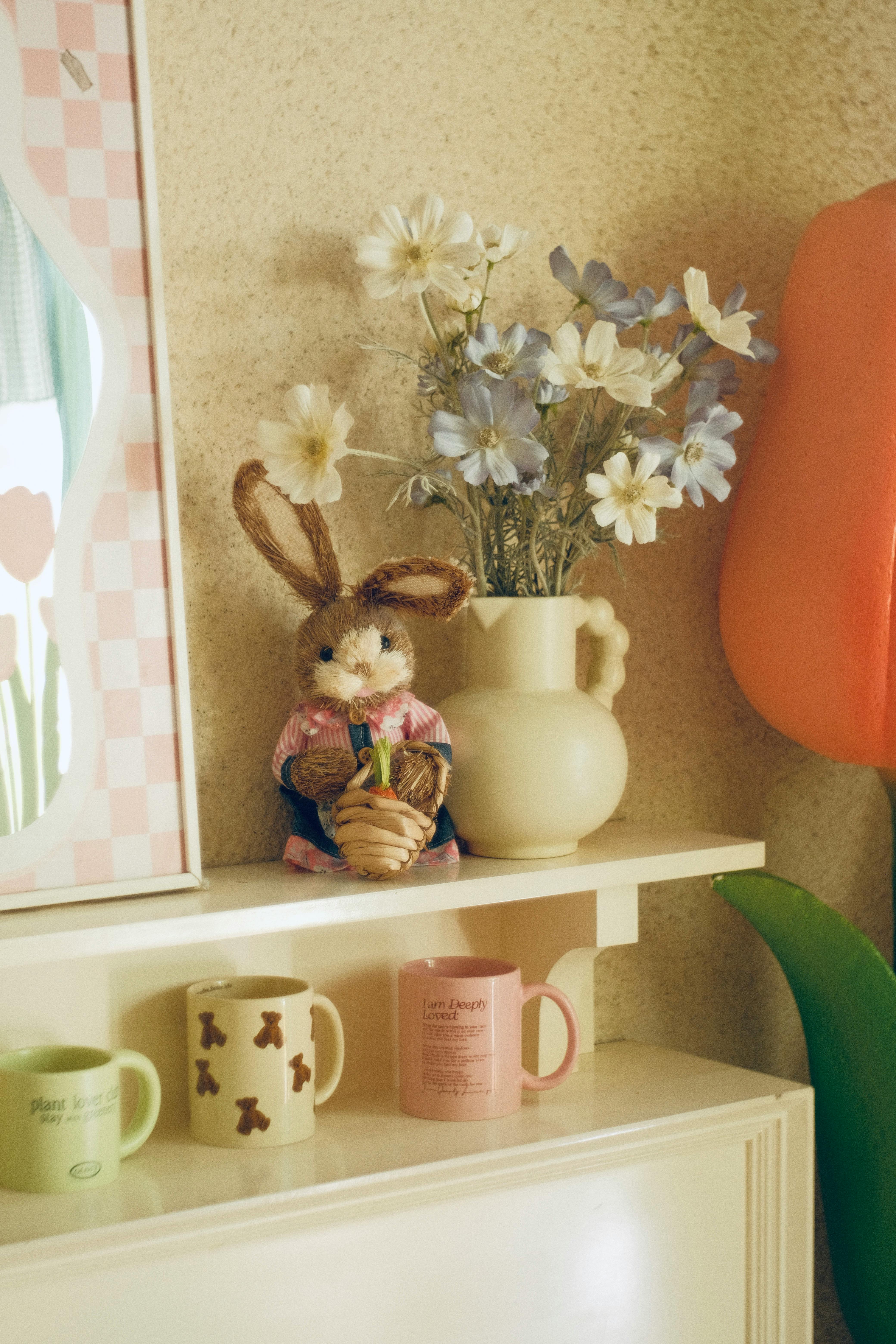 A shelf with flower arrangement, toy rabbit, and colorful mugs creating a cozy ambiance.