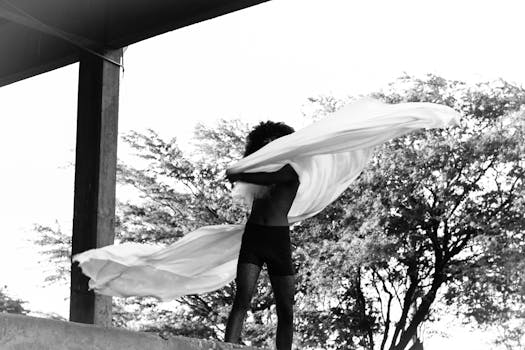 Male fashion model poses dynamically in black and white outdoor photoshoot.