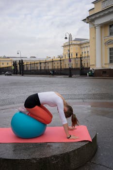 A woman practices stretching on a yoga ball in an urban city square, promoting fitness outdoors.