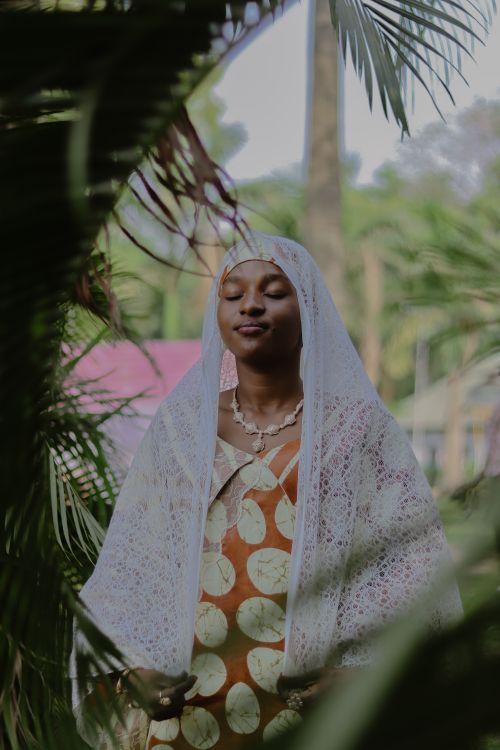 Free A serene woman in traditional African attire, surrounded by lush greenery. Stock Photo