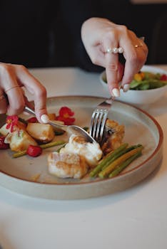 A close-up of a hands cutting an elegant plated fish dinner with vegetables.