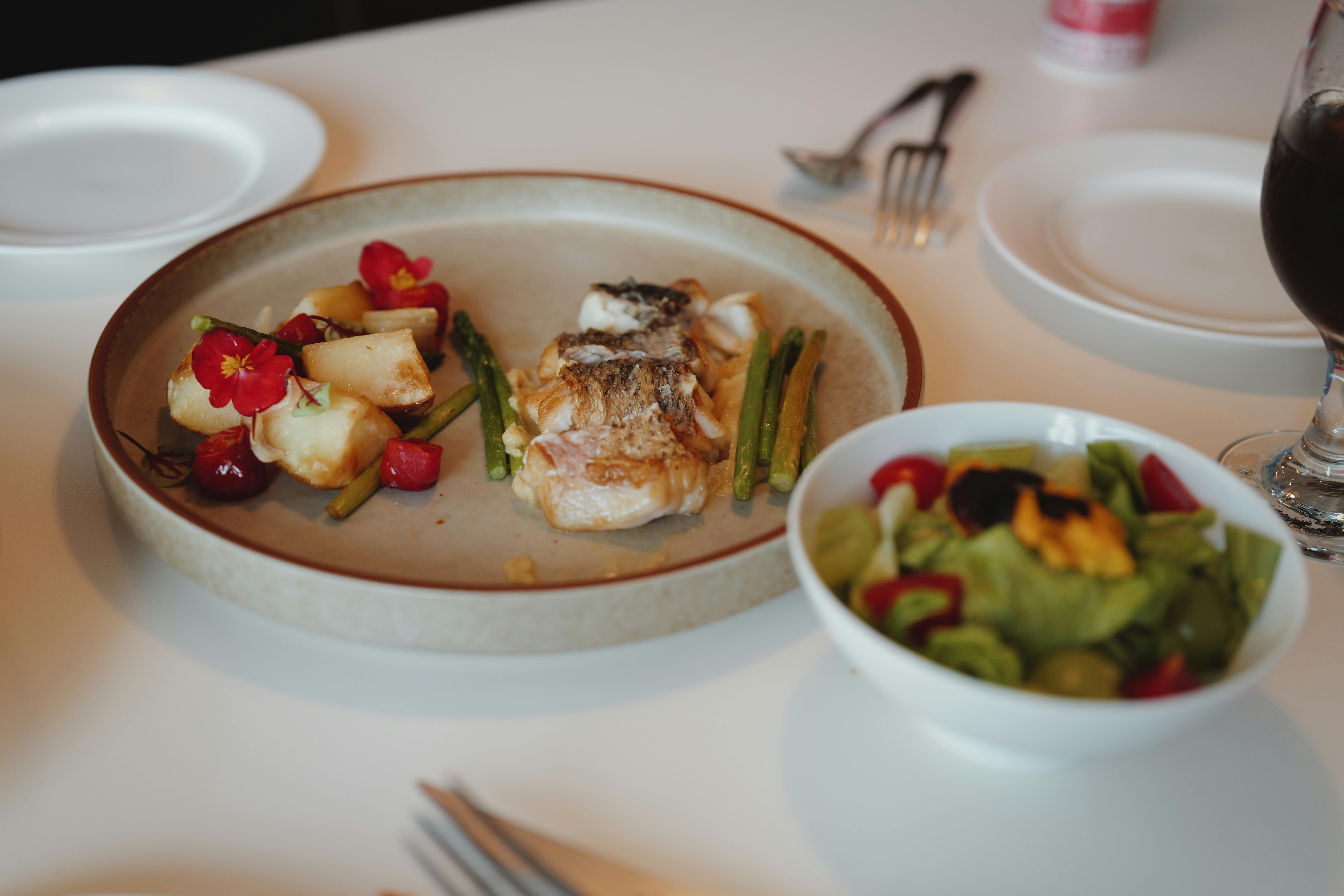 A gourmet dish with fish, vegetables, and a fresh salad served on a white table.