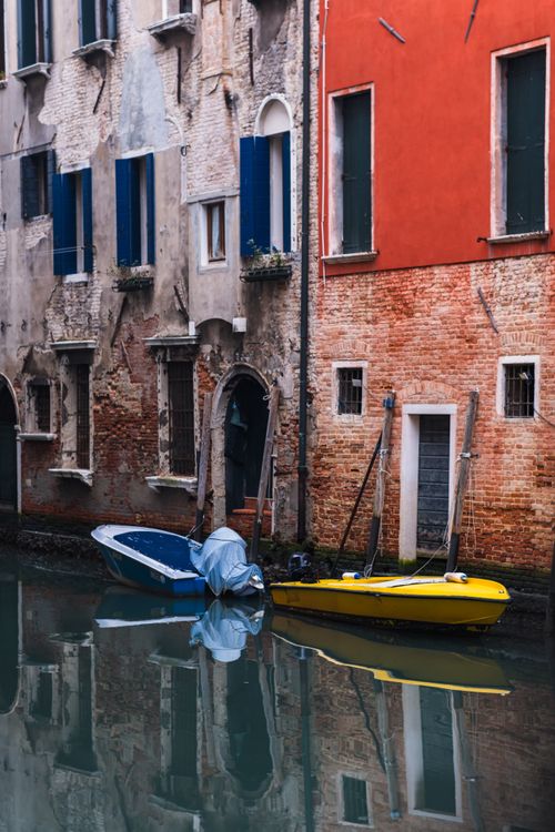 Free A picturesque Venetian canal scene with colorful rustic buildings and two moored boats. Stock Photo