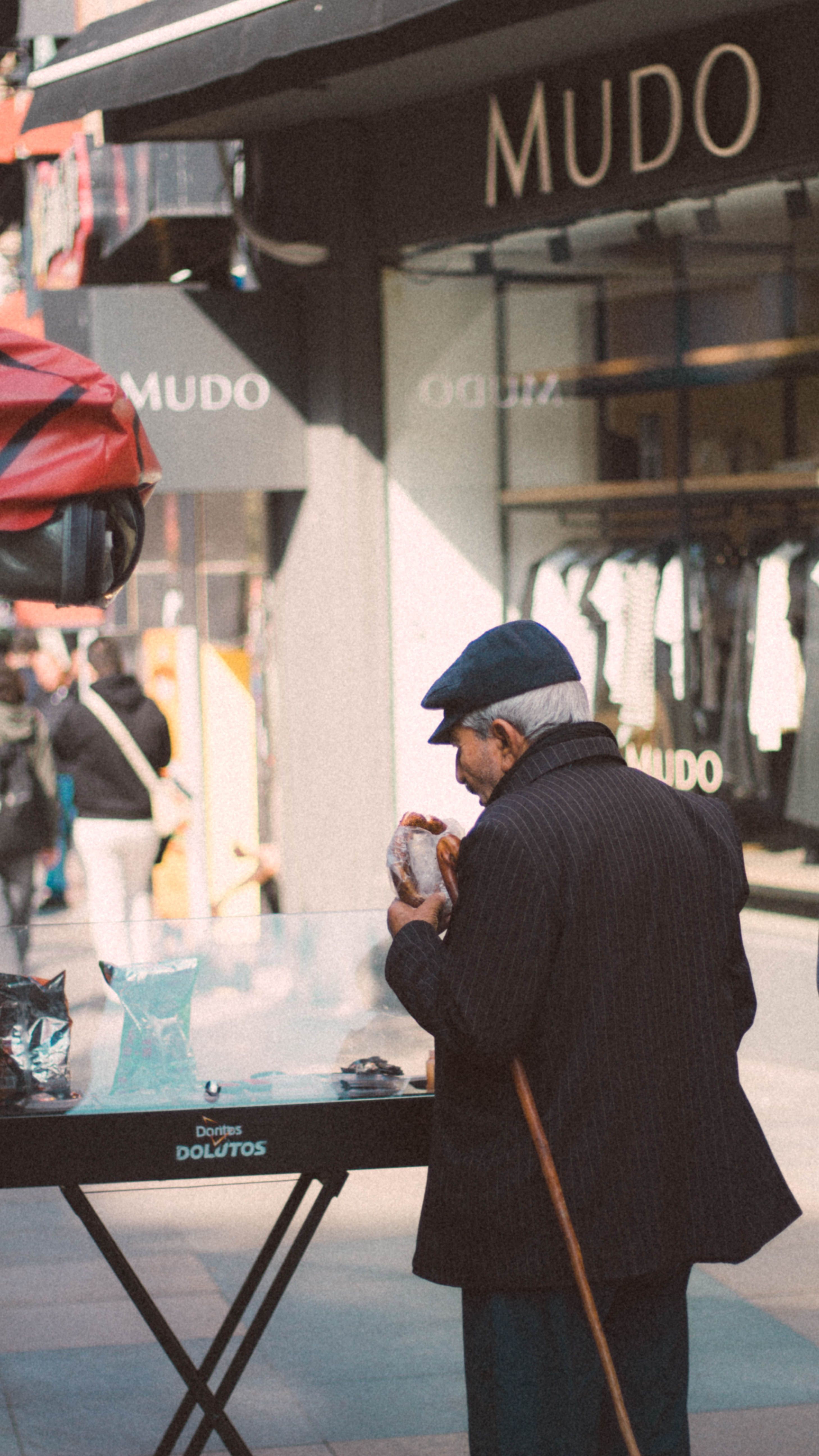 An elderly man enjoys a snack in front of a shop in Istanbul's busy street, capturing city life.