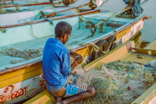 Free Fisherman mending net on boat in Kerala, showcasing traditional fishing practices. Stock Photo
