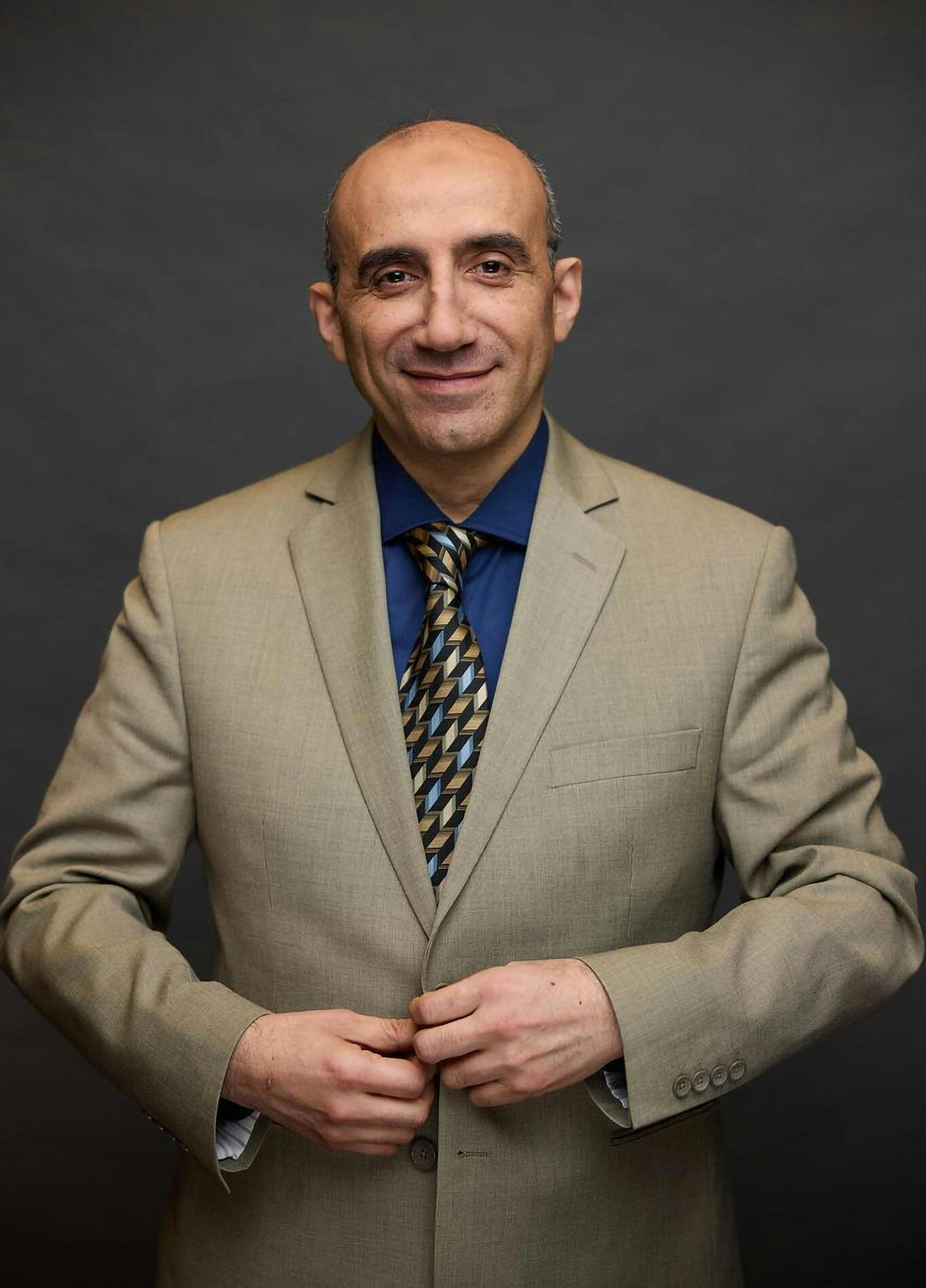 Confident man in a beige suit with a blue shirt and patterned tie.