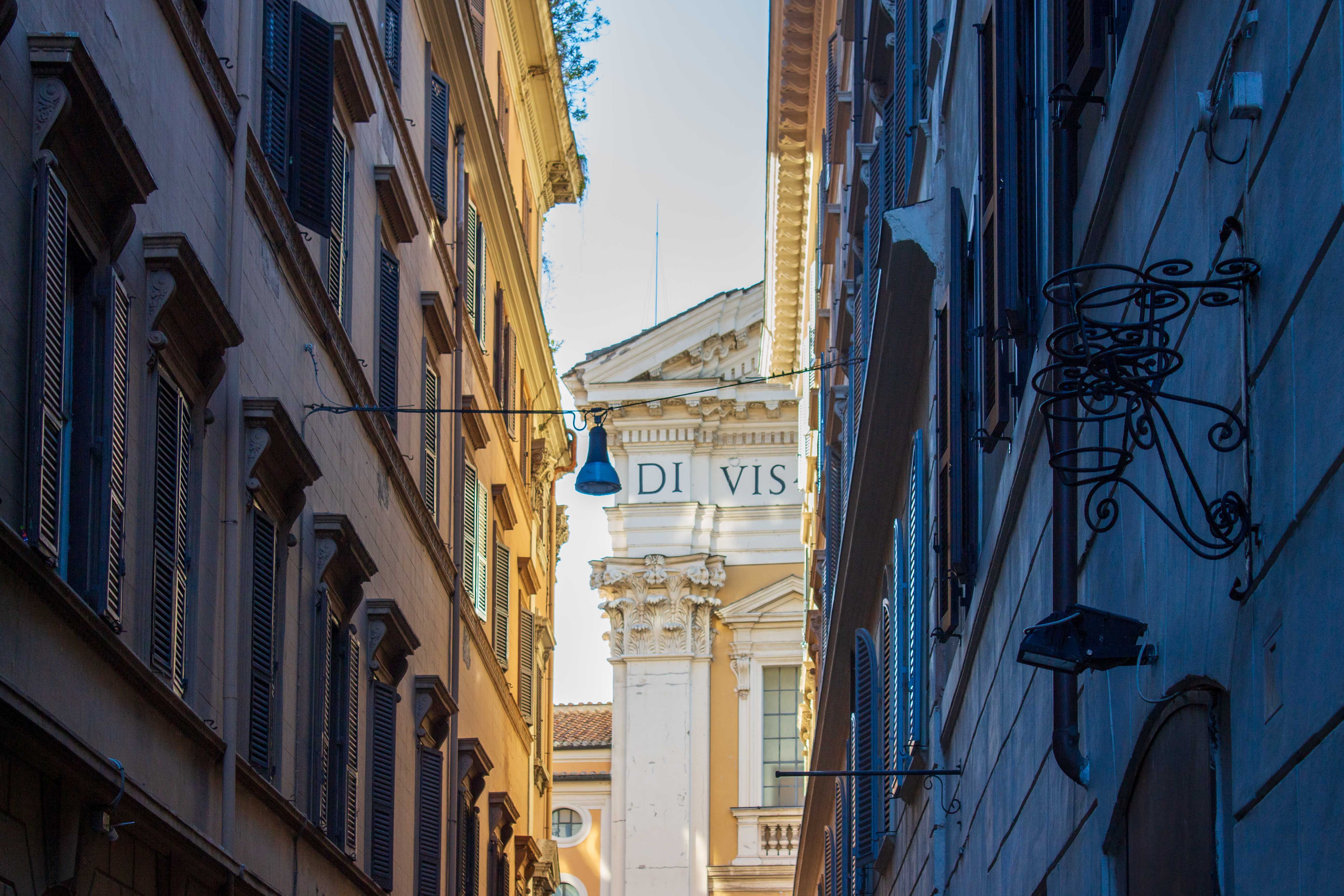 Narrow street in Rome showcasing historical architecture with beautiful facades and sunlight filtering through.