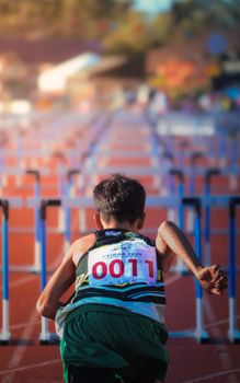 A young runner with numbered bib preparing for a hurdle race on a sunny track. — photo by kes Belnas