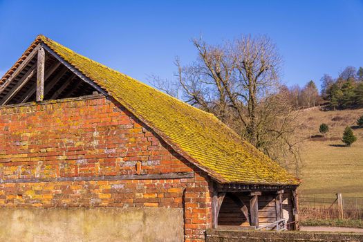 Charming old brick barn with moss-covered roof set in a picturesque rural landscape.