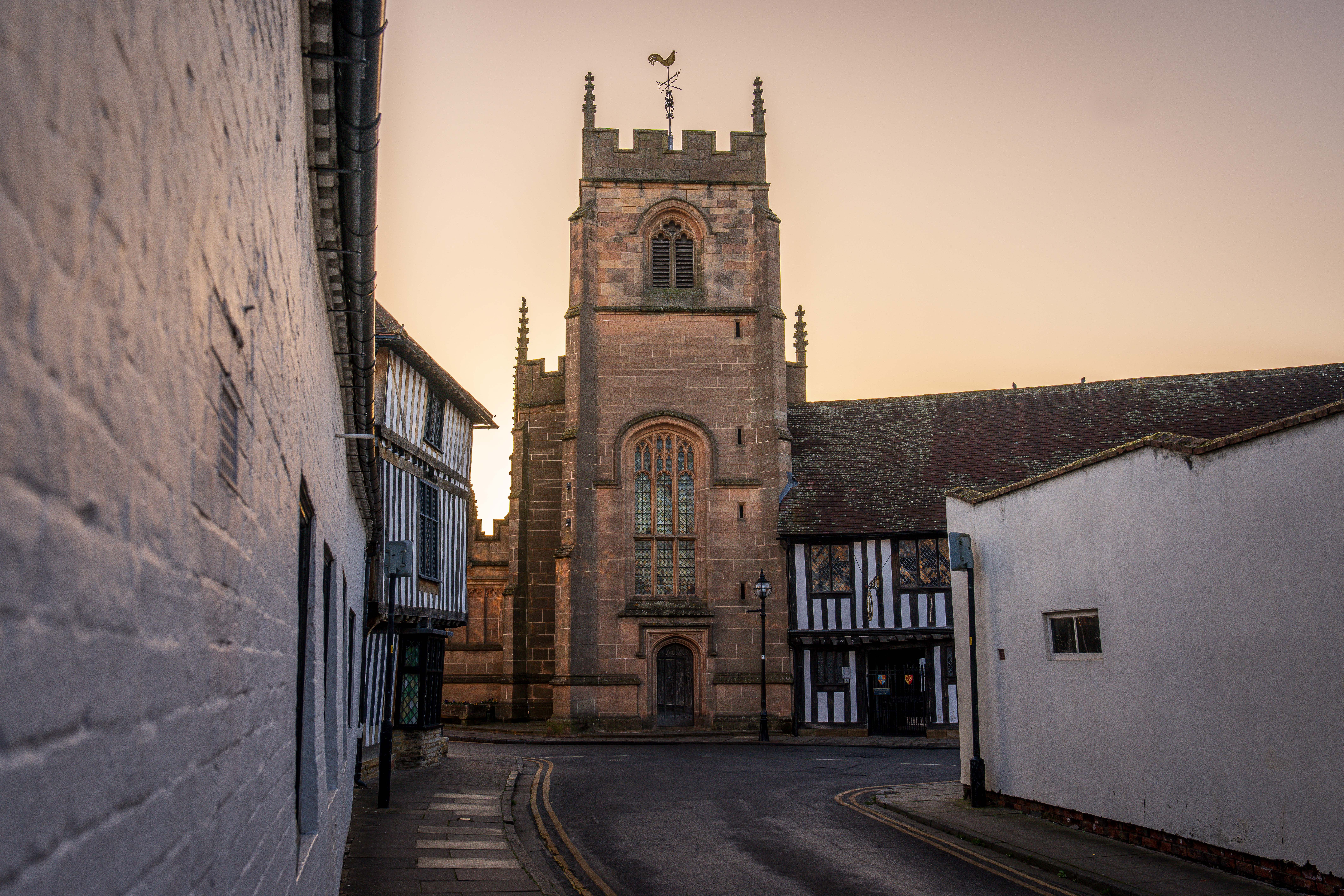 Charming church tower surrounded by historic buildings during sunset in a quaint village street.