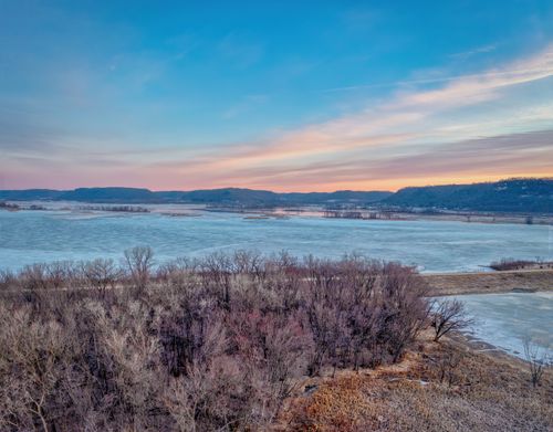 Free Aerial view of an icy river with surrounding winter landscape at sunset. Stock Photo