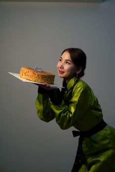 Smiling woman in green dress holding a birthday cake indoors.