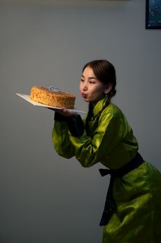A woman in green attire holding a cake and making a wish indoors.