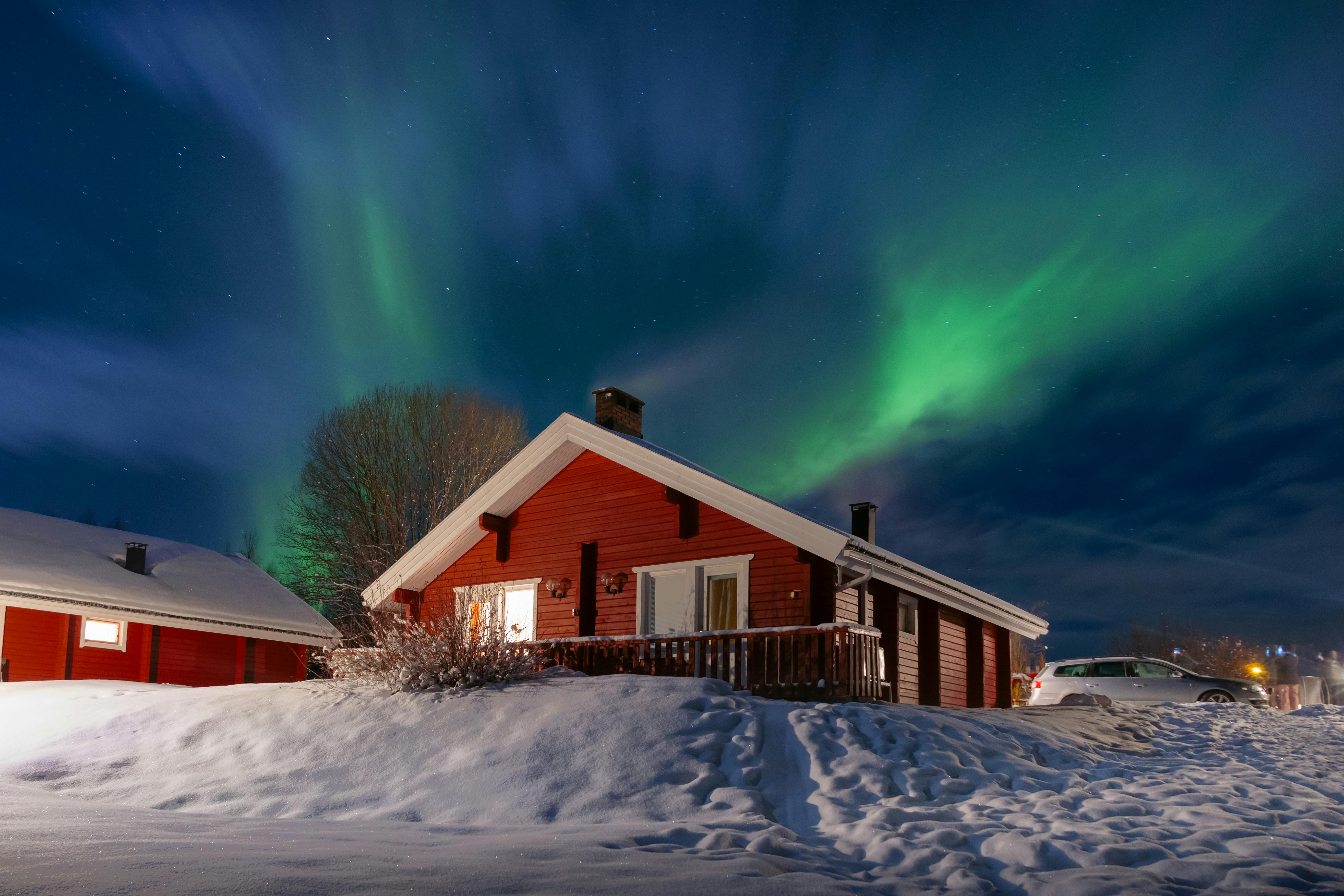 Red Finnish cottage under the Northern Lights in a snowy winter night scene.