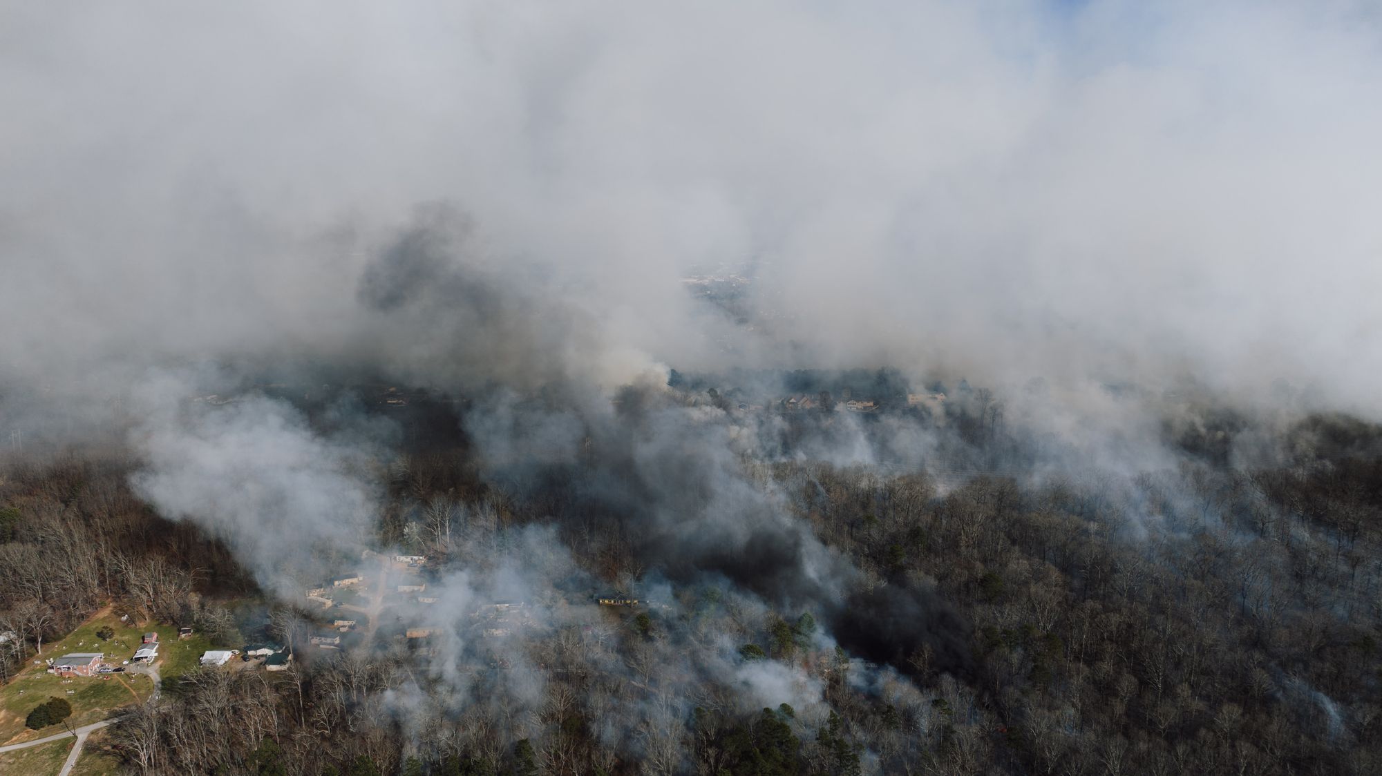 Columna de humo elevándose sobre un bosque de pinos bajo un cielo anaranjado