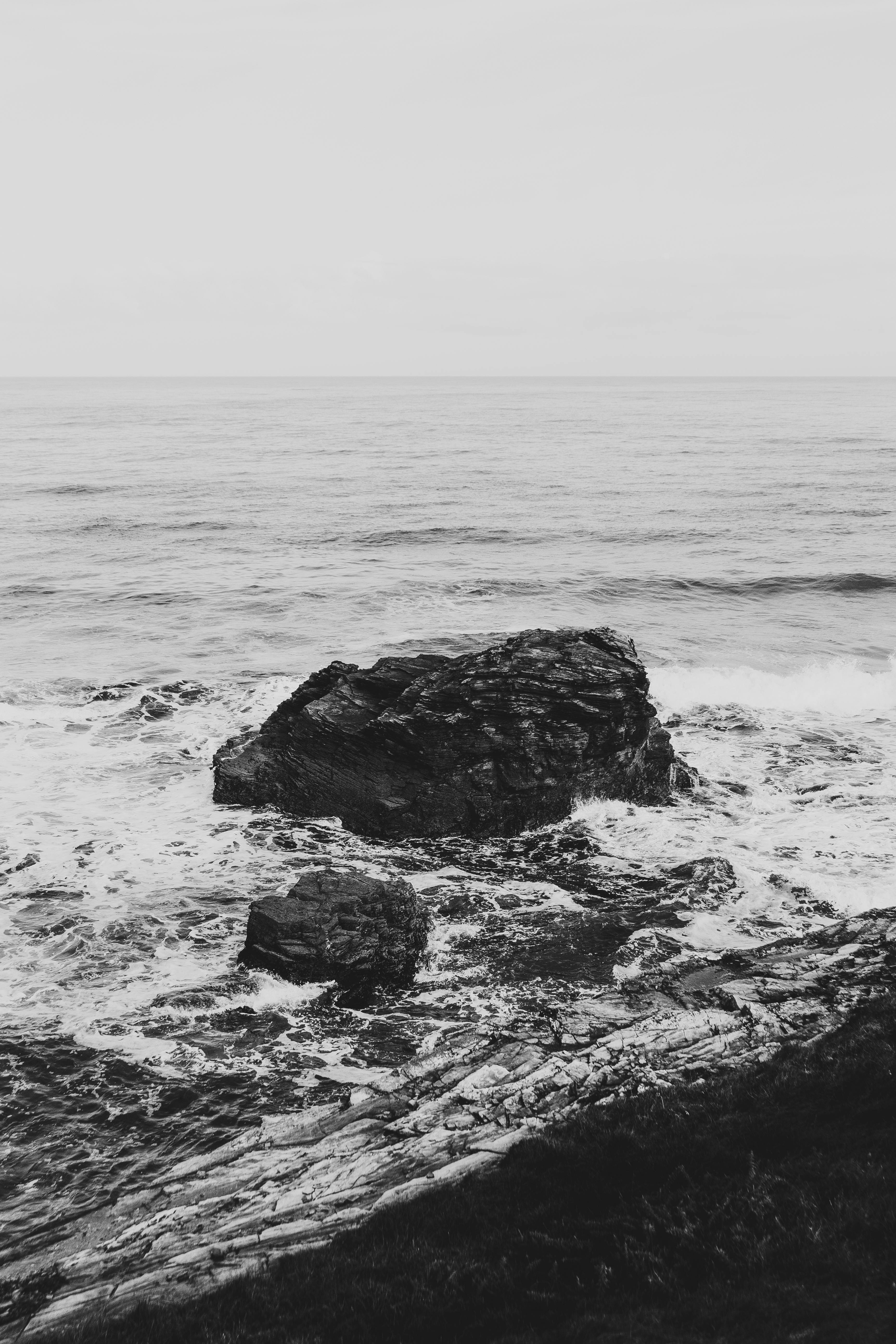 Black and white photo capturing ocean waves crashing onto rugged rocks, creating a dramatic seascape.
