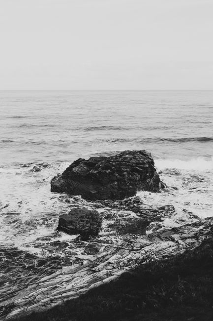 Black and white photo capturing ocean waves crashing onto rugged rocks, creating a dramatic seascape.