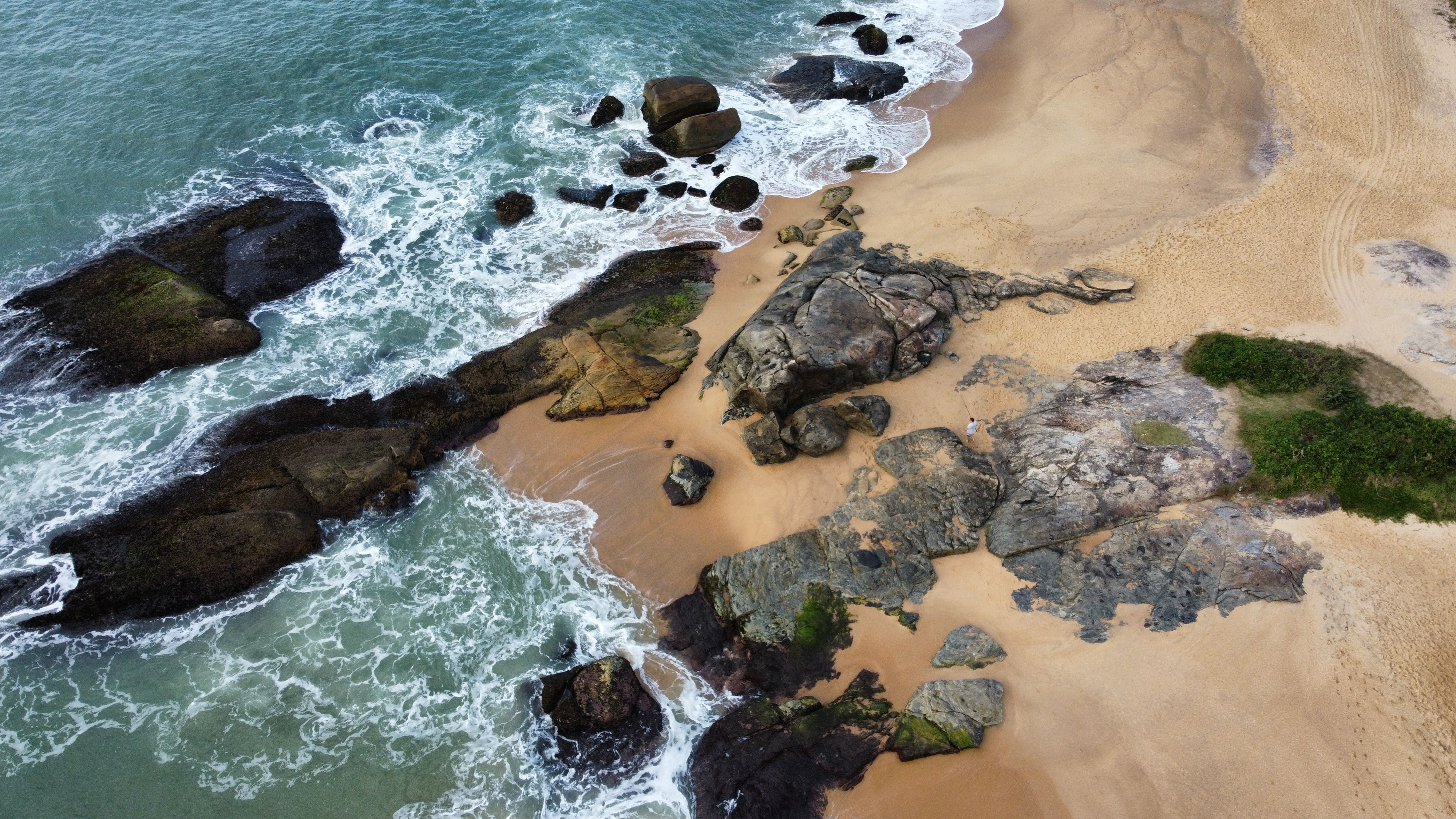 Aerial photo of a rocky shoreline and ocean waves in Santa Catarina, Brazil.