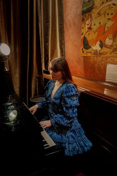 Stylish woman in a blue dress plays the piano, surrounded by artistic decor, creating a moody and aesthetic ambiance.