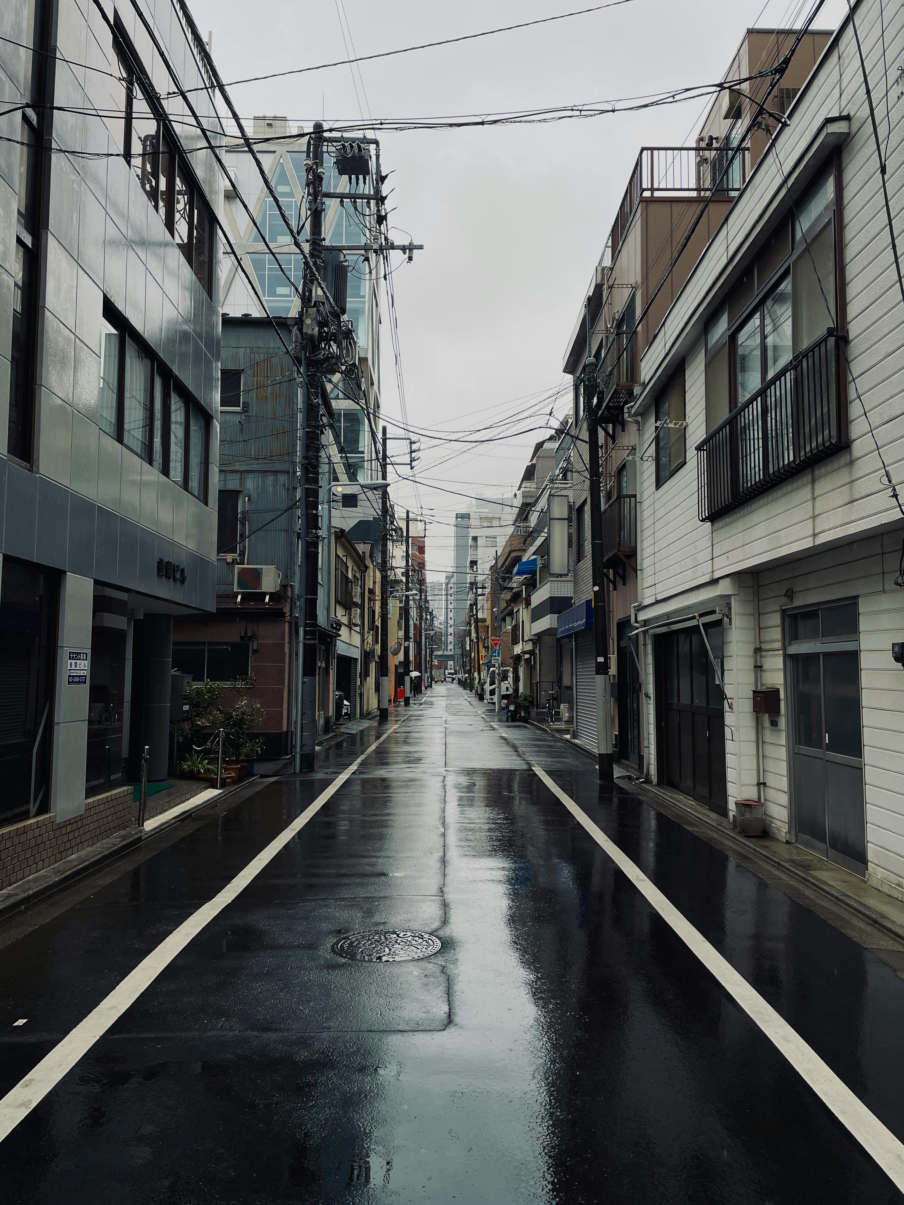 Quiet Tokyo street on a rainy day, showcasing wet roads and urban architecture.