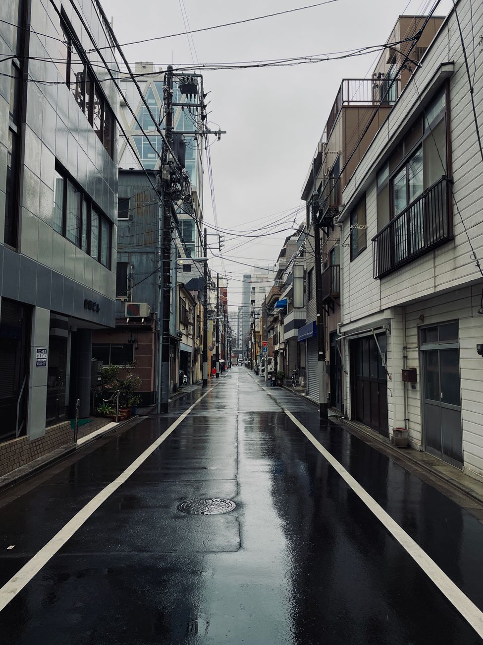 Stille straat in Tokio op een regenachtige dag, met natte wegen en stedelijke architectuur.